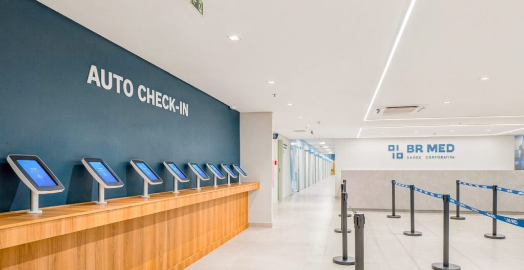 Área de auto check-in da BR MED com totens de autoatendimento sobre bancada de madeira