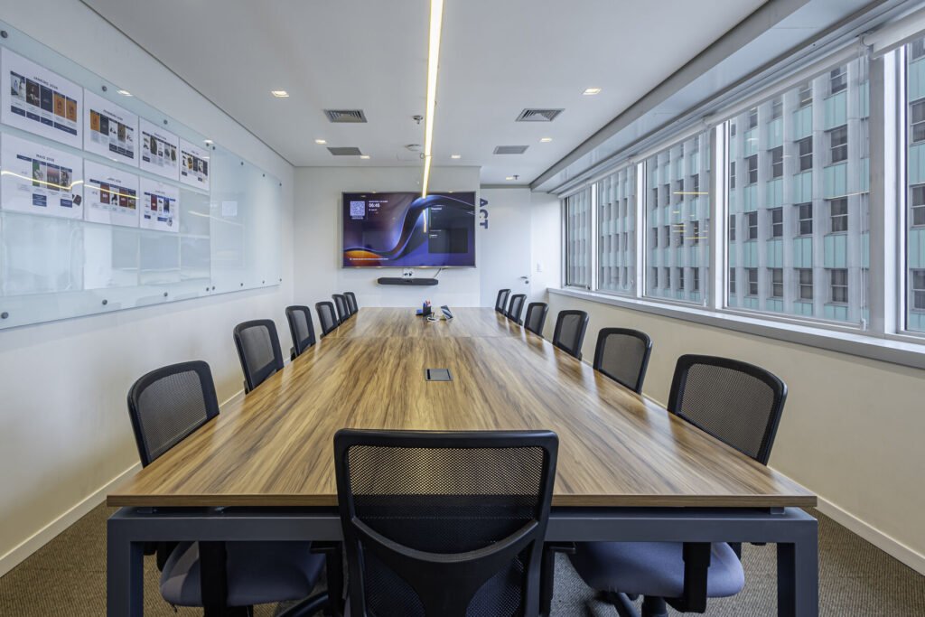Sala de reunião da MR.CAT com mesa longa de madeira, TV e vista para o Centro do Rio