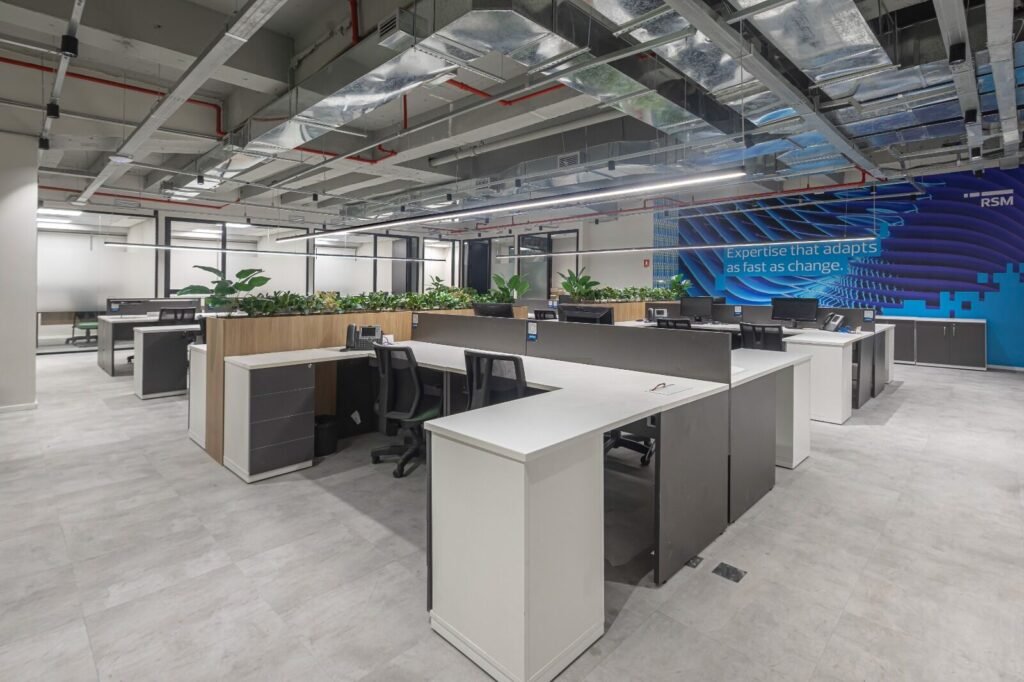 Open office da RSM com teto aparente e painel azul ao fundo